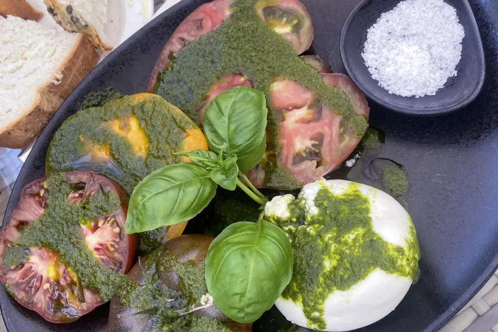 Plate of basil pesto with fresh mozzarella, heirloom tomatoes, and basil leaves, accompanied by fresh bread and sea salt at Friðheimar restaurant.